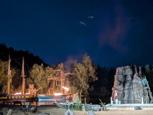 Ein beleuchtetes Schiff neben einem großen Felsen unter einem nächtlichen Himmel.